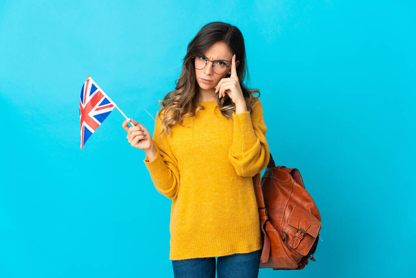 Birleşik Krallık bayrağını taşıyan genç İspanyol bir kadın mavi arka planda izole edilmiş bir fikir düşünüyor. - Fotoğraf, Görsel