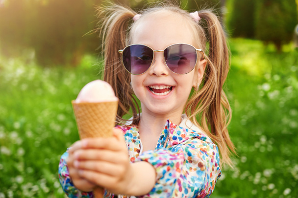 Το γελαστό κορίτσι περιποιείται το παγωτό και του κρατάει το χέρι. Καλοκαιρινό επιδόρπιο και θερινή ώρα - Φωτογραφία, εικόνα