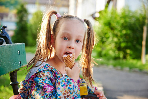 Niña con helado en cono de gofre está sentada en un banco al aire libre. Concepto de vacaciones, vacaciones y hora de verano - Foto, Imagen
