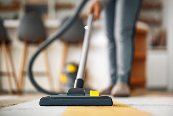 Mujer usando una aspiradora mientras limpia alfombras en la casa. - Foto, imagen