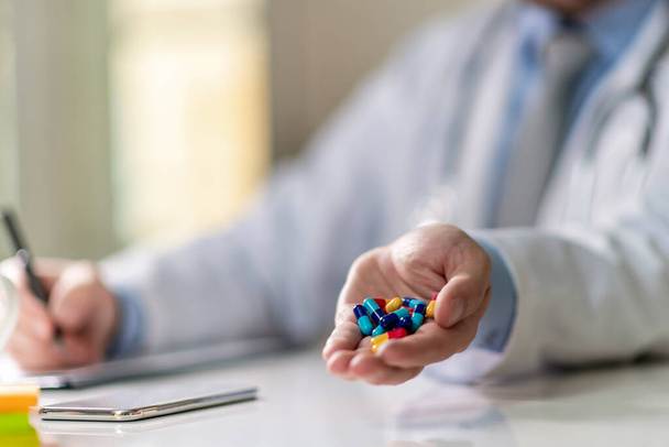 De cerca. Doctor mostrando pastillas en su oficina mientras escribe en documentos. - Foto, Imagen