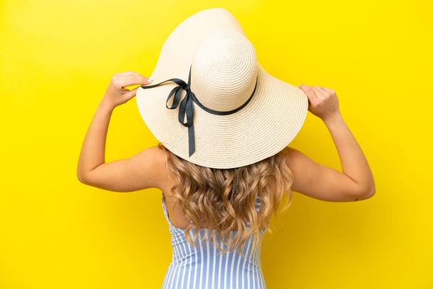 Young caucasian woman isolated on yellow background in swimsuit and in back position - Foto, Bild