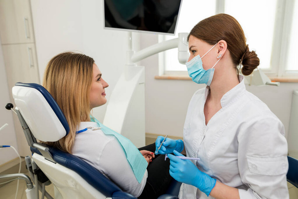 A female dentist is talking to a patient sitting in a dental chair. Dentist's consultation. - Foto, imagen
