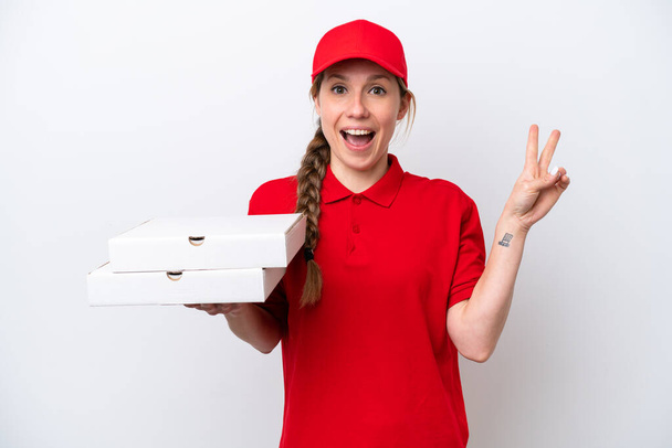 Pizza dağıtan kadın iş üniformalı beyaz arka planda izole edilmiş pizza kutuları alıyor gülümsüyor ve zafer işareti gösteriyor. - Fotoğraf, Görsel