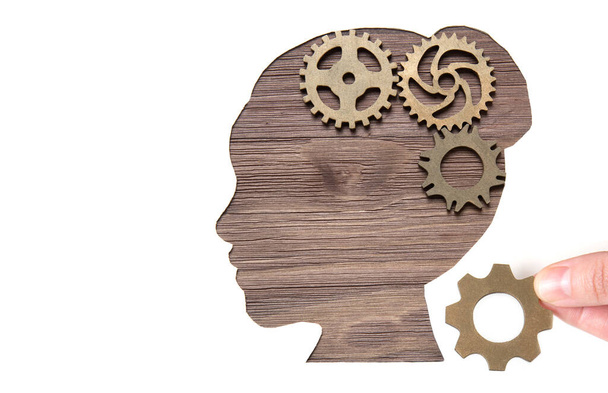 Hand placing gears in a head shaped paper cutout on a wooden background. Problem solving concept. - Foto, afbeelding