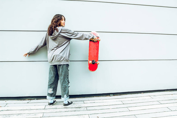 young skater woman on her back holding red skateboard on the street - Fotoğraf, Görsel
