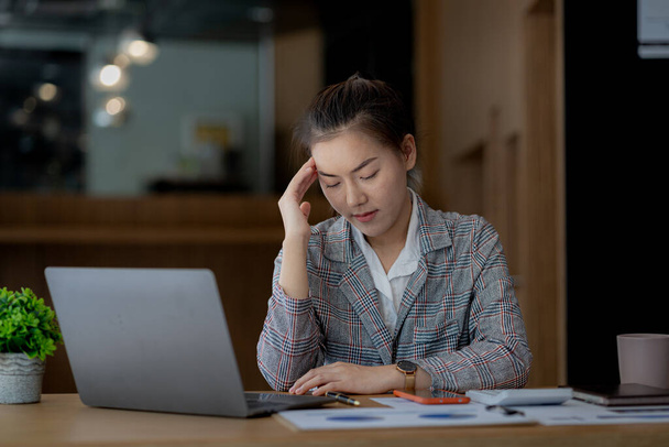 Beautiful Asian woman working in an office, she is a businesswoman who owns a company, she has a headache due to long and large paperwork leaving her tired and dizzy. The concept of sickness from work - Foto, Bild