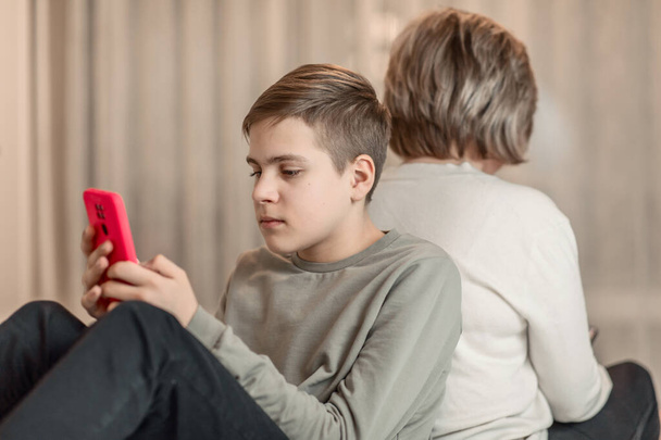tinédzser fiú és anya ül az ágyon háttal és nézi okostelefonok, a koncepció a virtuális kommunikáció a szociális hálózatok, időpocsékolás és elválasztás a való világtól - Fotó, kép