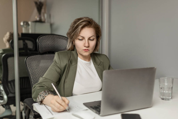 attractive, focused, middle-aged blonde, working on a laptop and with documents, work manager, entrepreneur - Foto, Imagen
