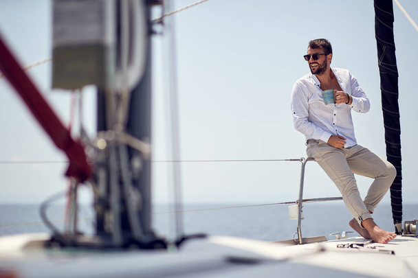 A young handsome barefoot male model is in a good mood while enjoying a photo shooting on a yacht on a beautiful sunny day on the seaside. Summer, sea, vacation - Foto, immagini