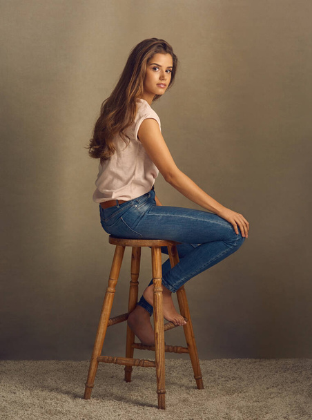 Be a perfectly put together mess if you want to. Studio shot of a beautiful young woman sitting on a stool against a plain background. - Foto, Bild