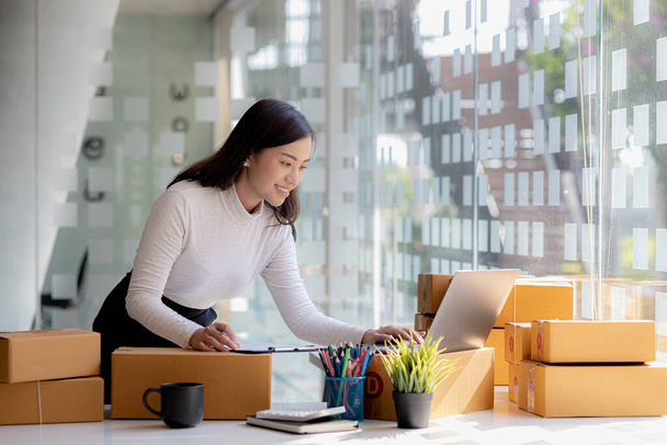 A beautiful Asian business owner opens an online store, she is checking orders from customers, sending goods through a courier company, concept of a woman opening an online business. - Photo, Image