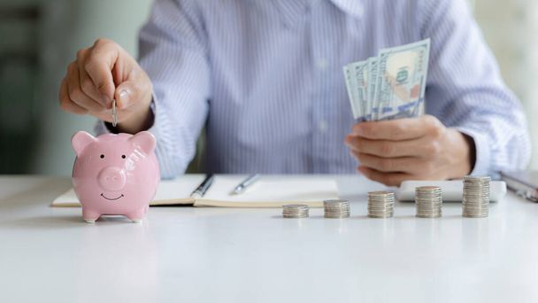 A businessman is putting coins into a pink pig piggy bank, he is saving for investments, money growth, stock investments. The idea of investing money to make it worthwhile to grow and be sustainable. - Foto, Imagen