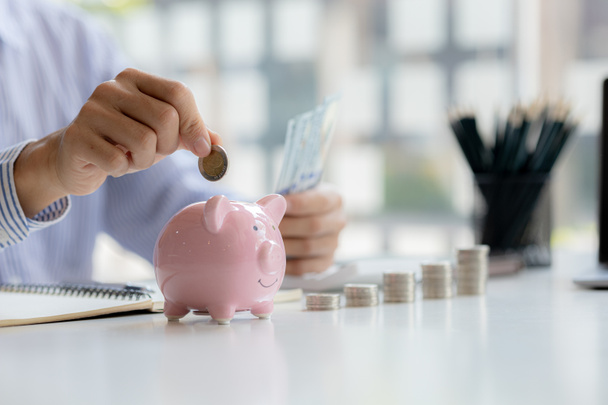 A businessman is putting coins into a pink pig piggy bank, he is saving for investments, money growth, stock investments. The idea of investing money to make it worthwhile to grow and be sustainable. - Photo, Image