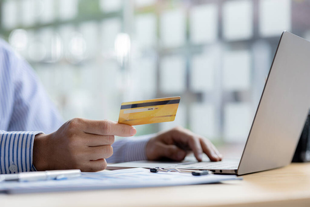 A person is holding a credit card to pay online, credit card payments can be used on both laptop computers and mobile phones. Concept of payment for goods and services via credit card. - Photo, Image