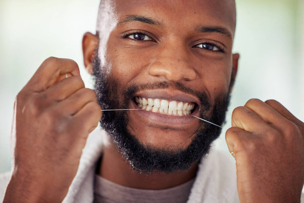Make flossing a part of your routine. Shot of a young man flossing his teeth at home. - Zdjęcie, obraz