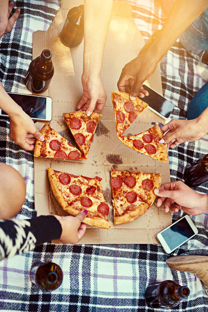 Jó kaja, nagyszerű barátok, dicső idők. Levágott kép egy baráti társaságról, akik pizzát esznek piknik közben.. - Fotó, kép