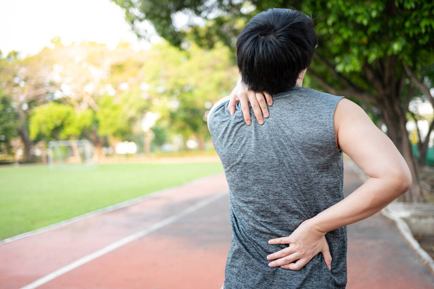 Боль в позвоночнике. Мужчина держит шею и спину, которые получили травмы во время прогулок в парке. Концепция спортивных травм - Фото, изображение