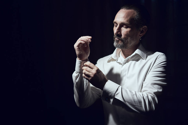 man fastens his cufflinks on sleeves on a white shirt on dark background - Foto, Bild