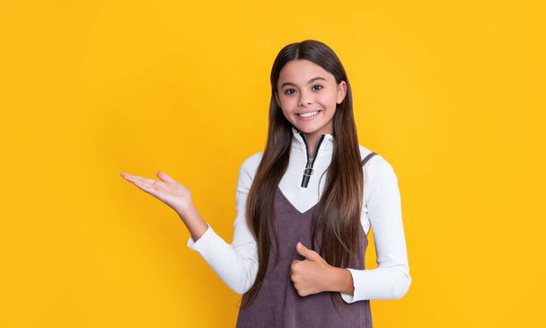 positive child with long hair on yellow background. presenting product - Foto, Bild