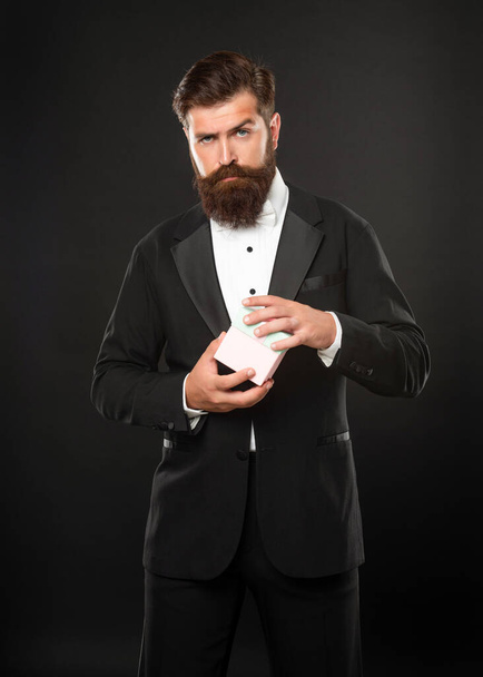 serious man in tuxedo bow tie formalwear on black background with gift box. boxing day - 写真・画像