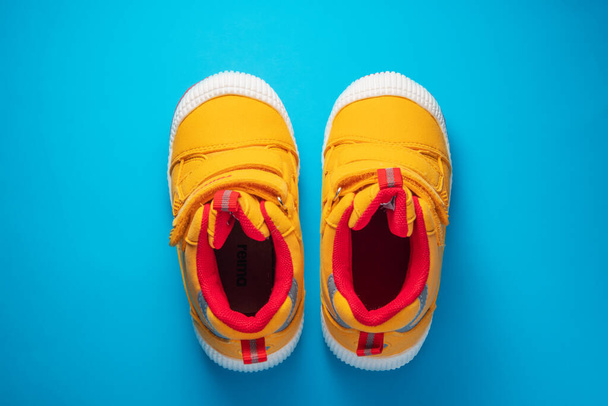 Yellow baby shoes. Kids sport sneakers isolated on blue background - Fotó, kép