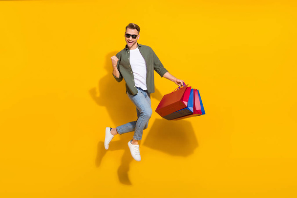 Full length body size view of attractive cheerful guy jumping buying gifts things rejoicing isolated over bright yellow color background - Fotografie, Obrázek
