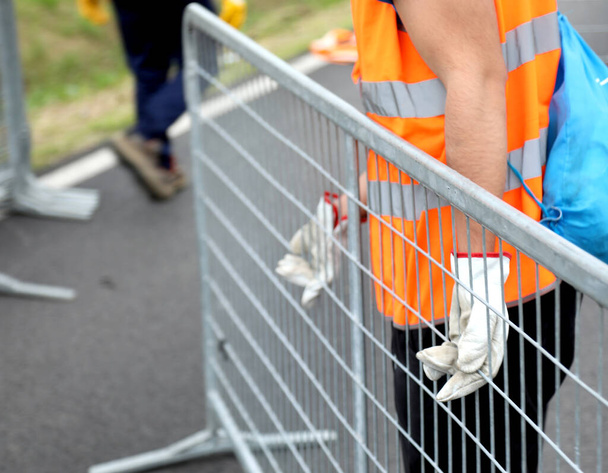 travailleur avec gilet réfléchissant et gants de travail tout en déplaçant la barrière de fer pour délimiter la zone réglementée - Photo, image