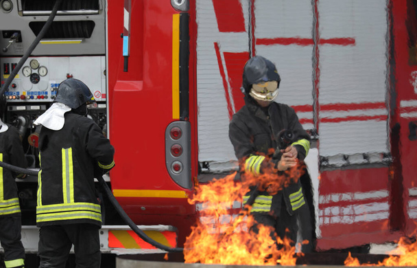 Firefighters drill with the fire truck and the fire to put out - Foto, afbeelding