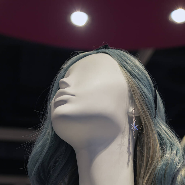 Beyaz bir kadın mankenin kafası, gri saçlı ve mor bir tavana dayanan gümüş küpeli spot ışıklarıyla. Moda mağazası. - Fotoğraf, Görsel