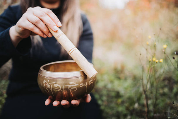 Black dressed woman outside holding and playing a tibetan singing bowl with a wooden stock. Selective focus - Foto, imagen