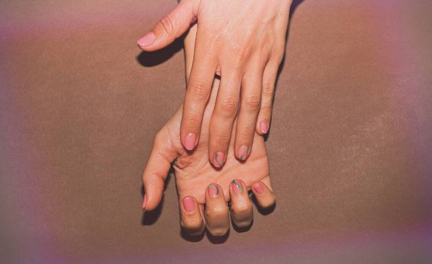 Mani di una bella donna ben curata con unghie femminili su uno sfondo marrone. Manicure, pedicure concetto di salone di bellezza. Spazio vuoto per testo o logo. Sulle unghie smalto gel bianco - Foto, immagini