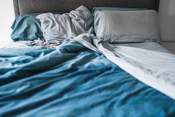 queen size bed lookng messy on one side and tidy on the other with light blue quilt cover and sheets, improving your sleep or couples life concept - Φωτογραφία, εικόνα