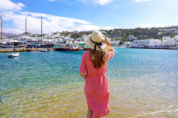 Holiday in Greece. Back view of young woman with hat and striped dress in Mykonos Island, Greece, Europe. - Foto, imagen