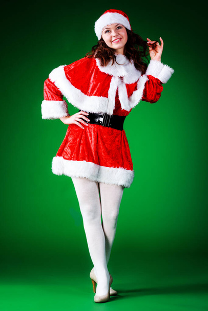 Uzun saçlı, Noel Baba gibi giyinmiş, yeşil krom arka planda poz veren güzel duygusal genç bir kız.. - Fotoğraf, Görsel