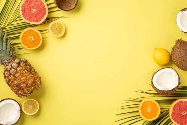 Summer concept. Top view photo of tropical fruits cracked coconuts cut oranges lemons grapefruits pineapple and palm leaves on isolated yellow background with copyspace - Фото, изображение