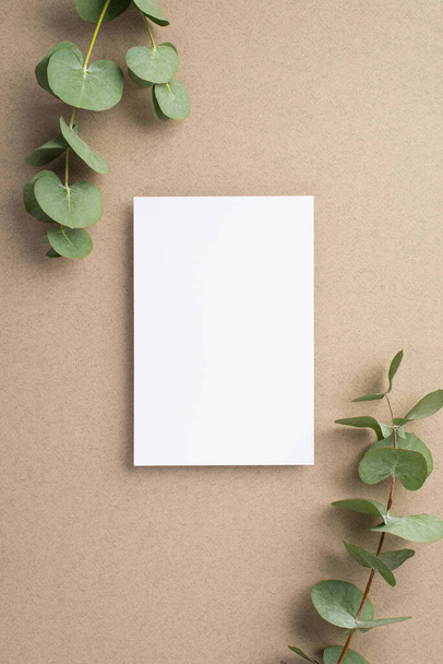 Business concept. Top view vertical photo of paper sheet and eucalyptus sprigs on beige background with empty space - 写真・画像