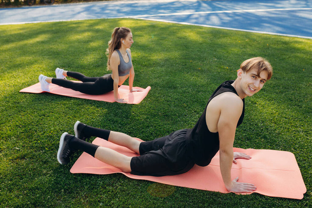 Photo of a beautiful happy couple in sportswear performing stretching exercises on a yoga mat - Photo, Image