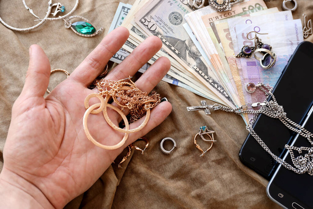 Marauders hand with bunch of stolen jewelry, money and smartphones on military uniform cloth fabric. Looting by Russian soldiers in the Ukrainian cities during the Russian invasion on Ukraine - Fotoğraf, Görsel