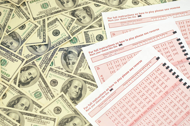 Pink gambling sheets with numbers for marking on big amount of hundred dollar bills. Lottery playing concept or gambling addiction. Close up photo - Фото, зображення