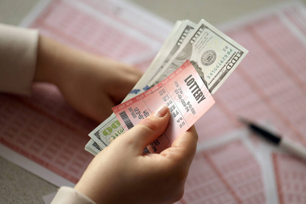A young woman holds the lottery ticket with complete row of numbers and dollar bills on the lottery blank sheets background. Lottery winner concept - Foto, imagen