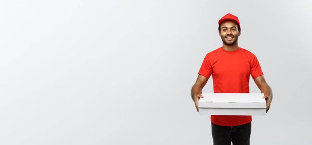 Conceito de entrega - Retrato de bonito afro-americano entregador de pizza. Isolado no estúdio Grey Background. Espaço de cópia
. - Foto, Imagem