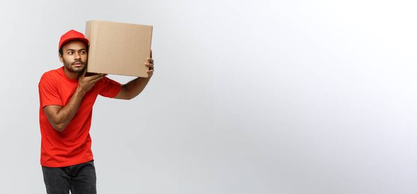 Delivery Concept - Portrait of Curious African American delivery man listen inside a box package. Isolated on Grey studio Background. Copy Space. - Foto, Imagem