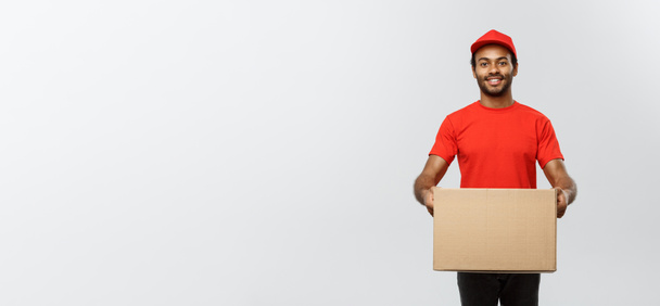 Toimitus Concept - Muotokuva Happy African American toimitus mies punaisella liinalla tilalla laatikko paketti. Eristetty Grey Studion taustalle. Kopioi tila. - Valokuva, kuva