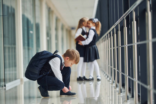 Boy sitting on the floor. School kids in uniform together in corridor. - 写真・画像