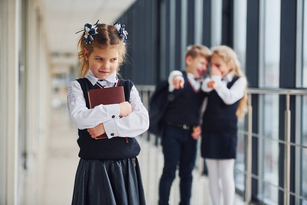 Little girl gets bullied. Conception of harassment. School kids in uniform together in corridor. - Photo, image