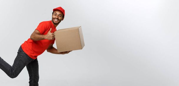 Levering Concept - knappe African American levering man rush uitgevoerd voor het leveren van een pakket voor de klant. Geïsoleerd op grijs studio achtergrond. Kopiëren van ruimte. - Foto, afbeelding