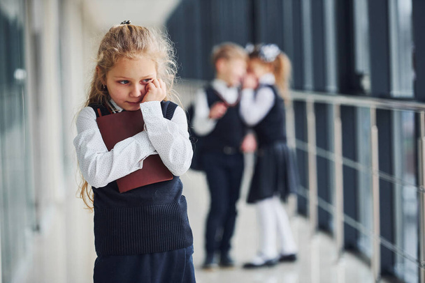 Little girl gets bullied. Conception of harassment. School kids in uniform together in corridor. - Фото, изображение