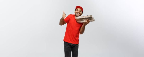 Concept de livraison - Portrait de beau livreur de pizza afro-américaine montrant le tonnerre. Isolé sur fond de studio Grey. Espace de copie
. - Photo, image