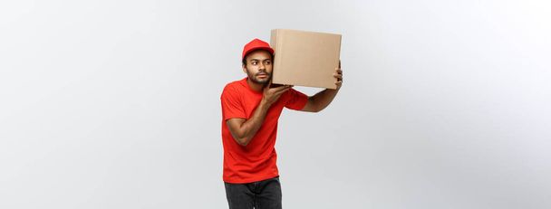 Teslimat kavramı - meraklı African American teslimatçı portresi bir kutu paket içinde dinle. Arka plan gri studio izole. Kopya alanı. - Fotoğraf, Görsel